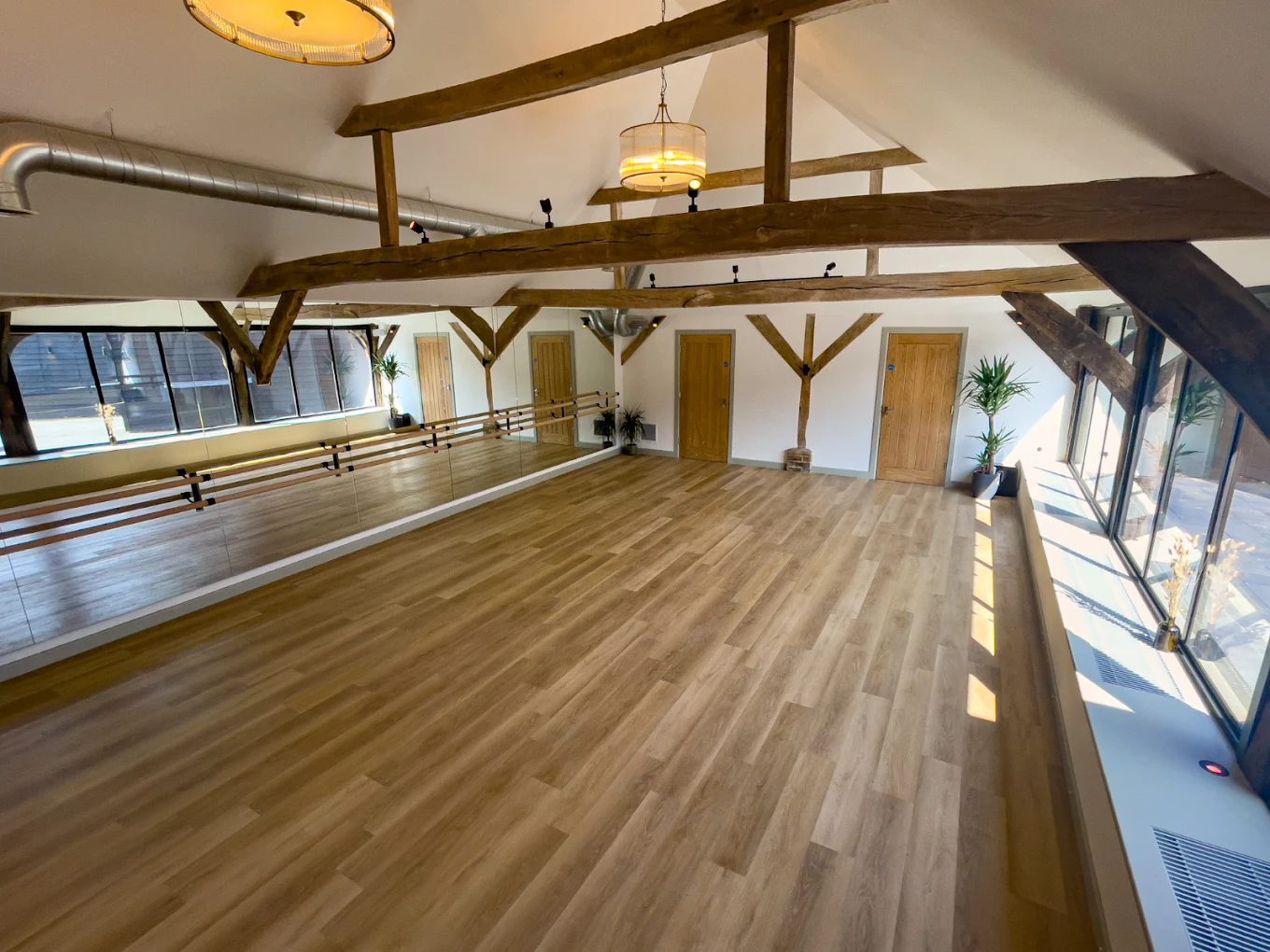 A studio beneath restored oak trusses, with barre and mirrors